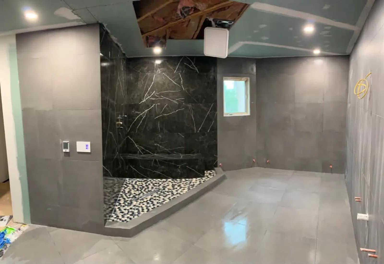 Large bathroom under construction with gray tile walls and a black marble shower