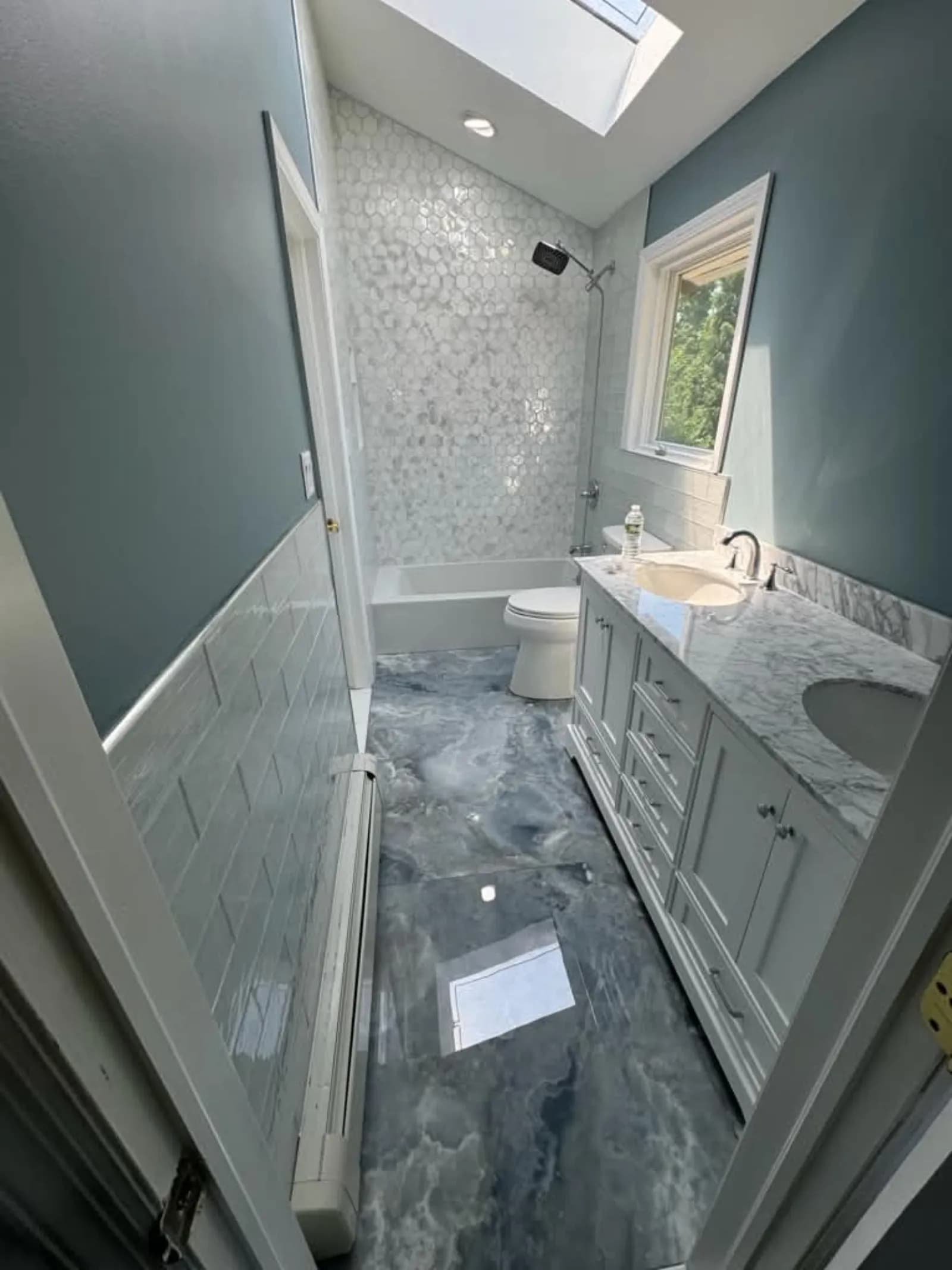 Bathroom with skylight, hexagon tile tub wall and a marbled blue epoxy floor