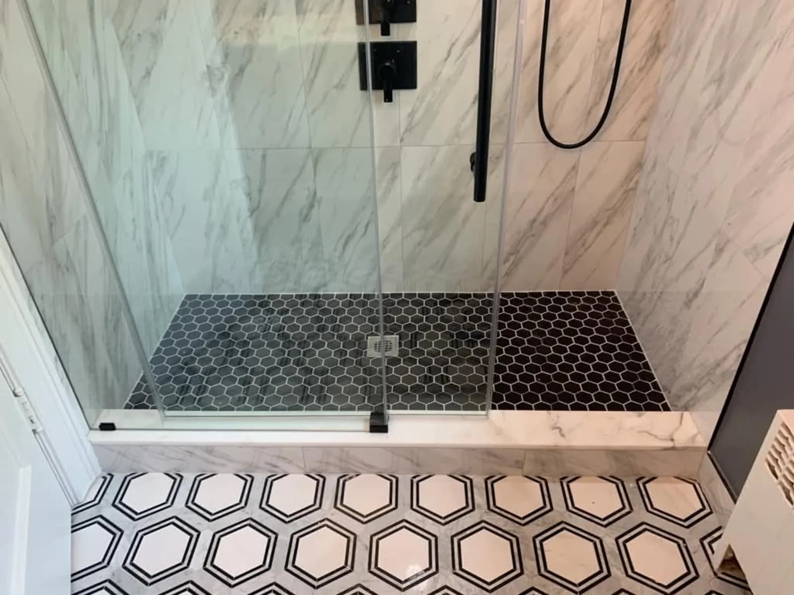 Shower with black hexagon pan and marble-look walls above a black-and-white hex tile floor